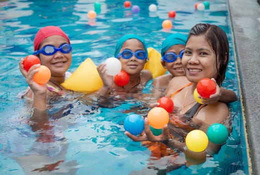 A portrait of a mother and her children playing ball in the pool.