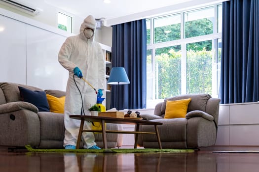 Asian Medical staff in personal protective equipment PPE suit spraying disinfectant spray for coronavirus COVID-19 in living room. Delivery health care hygiene and disinfection concept