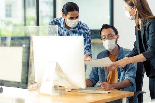 Three asian business person discuss their work in morning after office reopen due to coronavirus COVID-19 pandemic. They wear protective face mask to prevent infection. New normal office life concept.