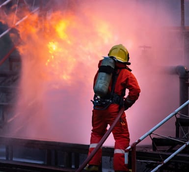 Firefighter using water fog type fire extinguisher to fighting with the fire flame from oil pipeline leak and explosion on oil rig and natural gas station. Firefighter and industrial safety concept.