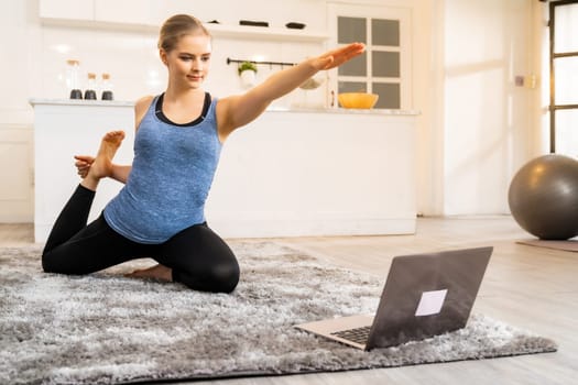 White caucasian fit sporty woman doing yoga king pigeon pose while working at home with laptop in living room while quarantine. Workout fitness sport healthy lifestyle and work from home concept.