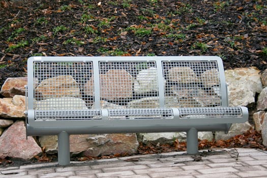 An iron resting bench in front of large natural stones.