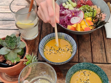 Woman eating tasty colorful healthy natural organic vegetarian Hawaiian poke bowl using asian chopsticks on rustic wooden table. Healthy natural organic eating concept.