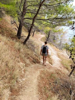 Young active feamle tourist wearing small backpack walking on coastal path among pine trees looking for remote cove to swim alone in peace on seaside in Croatia. Travel and adventure concept.