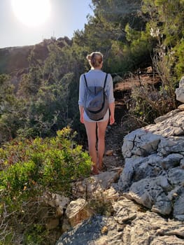 Young active feamle tourist wearing small backpack walking on coastal path among pine trees looking for remote cove to swim alone in peace on seaside in Croatia. Travel and adventure concept.