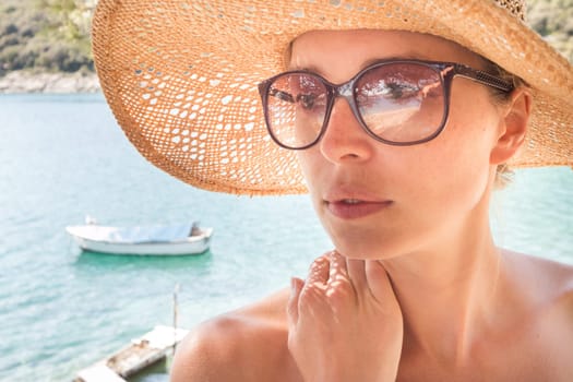 Close up portrait of no makeup natural beautiful sensual woman wearing straw sun hat and sunglasses on the beach in shade of a pine tree.