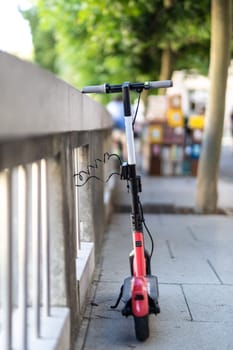 Red electric scooter parked and safely chained to a fence. Eco friendly green modern urban mobility concept of sharing transportation with electric scooters for rent in Ljubljana, Slovenia.