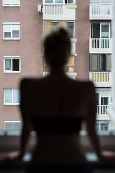 Home quarantine and social distancing during covid pandemic. Silhouette of lonley caucasian woman standing by window, anxiously looking out. Coronavirus infection, pandemics, disease outbreaks.