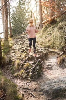 Active sporty woman listening to the music while running in autumn fall forest. Female runner training outdoor. Healthy lifestyle image of young caucasian woman jogging outside.
