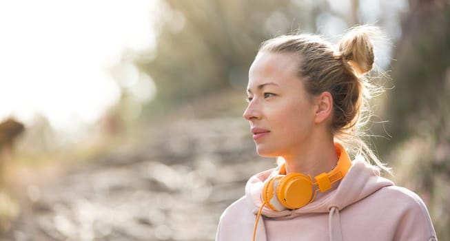 Portrait of beautiful sports woman with hoodie and headphones during outdoors training session. Healthy lifestyle image of young caucasian woman jogging outside.