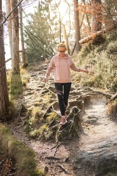 Active sporty woman running in autumn fall forest jumping over the roots on the path. Healthy lifestyle image of young active caucasian woman jogging outside in nature.