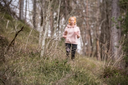 Active sporty woman listening to the music while running in autumn fall forest. Female runner training outdoor. Healthy lifestyle image of young caucasian woman jogging outside.