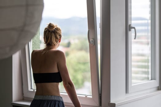 Home quarantine and social distancing during covid pandemic. Silhouette of lonley caucasian woman standing by window, anxiously looking out. Coronavirus infection, pandemics, disease outbreaks.