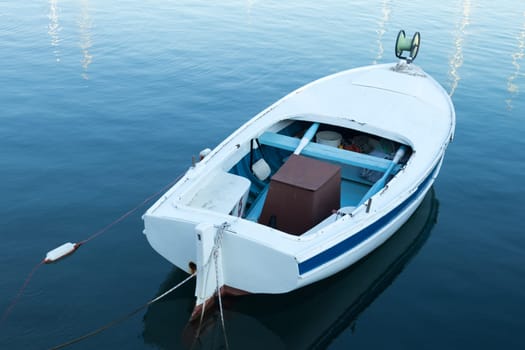Vintage old white wooden row boat on blue sea water.