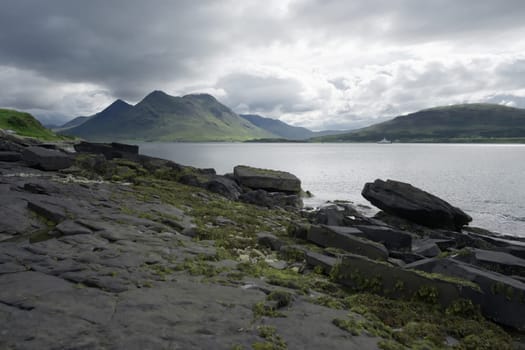 Coastal landscape from the isle of raasay looking towards the isle of skye. Ferry travels the sea under the peak of Glamaig which is cloud topped.