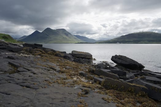 Coastal landscape from the isle of raasay looking towards the isle of skye. Ferry travels the sea under the peak of Glamaig which is cloud topped.