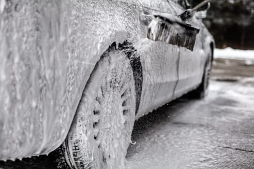 Detail on car and wheel, covered with lot of soap, brush spraying more shampoo foam, when being washed in carwash.