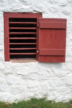 Whitewashed  stone barn with red slatted ventilation window and open shutter in a grassy field. Rustic charm and beauty in natural light with copy space.