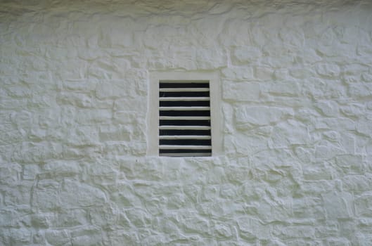 Old slatted ventilation window in a whitewashed stone wall on historic farm. Full frame rustic image in natural light with copy space.