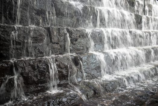 Full frame long exposure image of a tiered waterfall, close up image shows movement and sction of water and rough heft of stone.