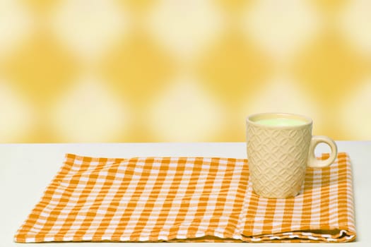 Empty breakfast table. Close-up of a yellow ceramic mug with milk on yellow checkered napkin or tablecloth on a abstract background. Template for your food and product display montage.