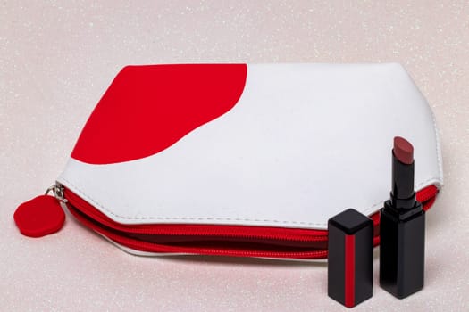 Table top on cosmetic background. Close-up of a beautiful opened red white cosmetic bag and an opened elegant red lipstick on a bright pink glittering background. Concept beauty. Macro.