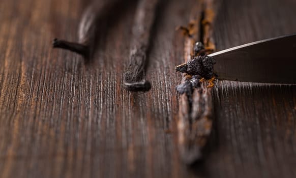 Vanilla beans and seed pods with knife on wooden background. Preparing vanilla as baking ingredient.