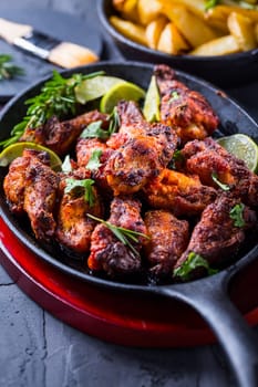Roasted chicken wings in barbecue sauce with lime and baked potatoes in rustic pan