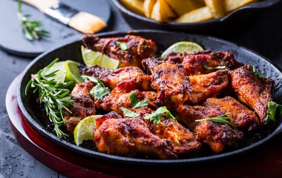 Roasted chicken wings in barbecue sauce with lime and baked potatoes in rustic pan