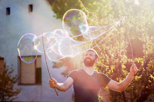 The playful bearded man is making giant soap bubbles on the street.