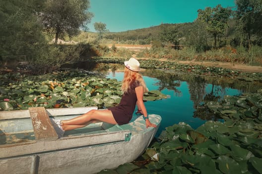 Carefree young woman floating relaxed on a boat at a pond with blooming waterlily, lotus flowers. Vacation travel, natural background at the lake with a beautiful fit girl sailing, at Bardar, Moldova.