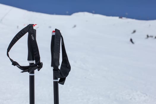 Detail on ski poles hand grip, with blurred piste with skiers and deep blue sky in background.