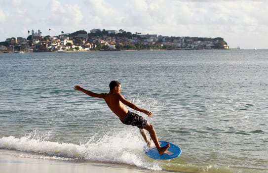 salvador, bahia / brazil - august 12, 2015: young man is seen surfing with a piece of wood on Ribeira beach in the city of Salvador.
