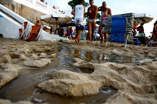 salvador, bahia / brazil - november 4, 2015: people are seen by the open sewage water gushing in the sand of Porto da Barra in the city of Salvador.