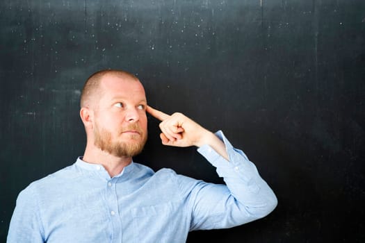 Handsome businessman standing at the empty blackboard with copy space.