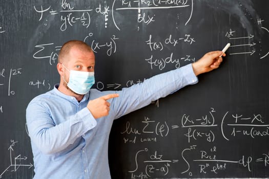 Male teacher with mask teaching math lesson at school. Social distanting and classroom safety during coronavirus epidemic