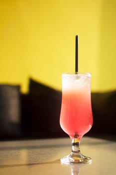 The red iced alcoholic fruity cocktail drink is on table on black and yellow background.