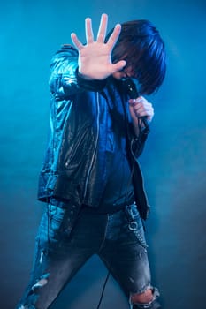 The young guy in black leather jacket is singing rock music and performing on the stage.