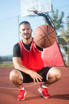The squatting young basketball player is showing the basketball ball as symbol of basketball sport.