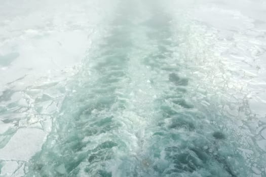 A trail on the water from the ship. Arctic and ice on the water. The propellers of the ship smeared the water.