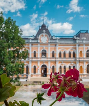 Close up of red flowers over the Manuc Bei mansion background. An architectural, culture and historic complex and museum, at Hincesti, Moldova. Manuc Bey palace facade and yard in a sunny summer day..
