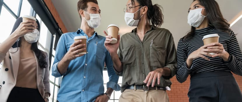 Panoramic group of business worker team with takeout coffee cup walking back to office after lunch break. They wear protective face mask in new normal office preventing coronavirus COVID-19 spreading.