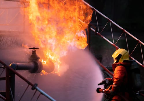 Firefighter using water fog type fire extinguisher to fighting with the fire flame from oil pipeline leak and explosion on oil rig and natural gas station. Firefighter and industrial safety concept.