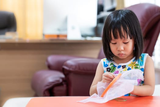 Asian girl child sewing in living room at home as home schooling while city lockdown because of covid-19 pandemic across the world. Home Schooling prepare for Preschool concept.