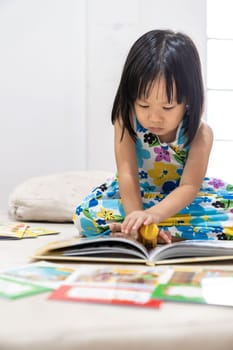Asian girl child reading interactive book in living room at home as home schooling while city lockdown because of covid-19 pandemic across the world. Home Schooling prepare for Preschool concept.