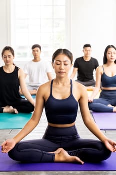 Group of sporty attractive asian people wearing sportswear bra pants practicing yoga lesson on Lotus pose position sitting Padmasana with instructor coach. Work out fitness healthy lifestyle concept