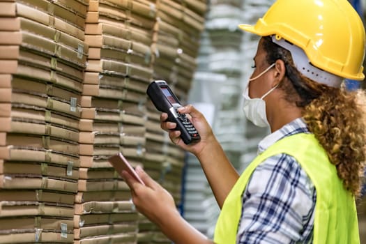 African black warehouse worker with face mask checking goods use digital tablet and barcode scanner, she wear face mask prevent from COVID-19 after factory reopen.