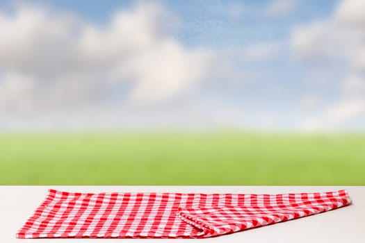 Empty table product. Closeup of a empty red checkered tablecloth or napkin on a bright table against abstract blurred summer background. Template for food and product display montage.