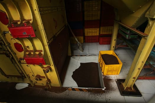 Dried tea in yellow plastic box, and some tea dust on the floor of tea manufacturing factory, in the dryer room. Kandy, Sri Lanka.