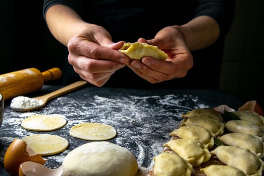 Cook in a dark jacket prepares dumplings. over a dark table on which the finished dumplings are laid out. Front views, close-up.